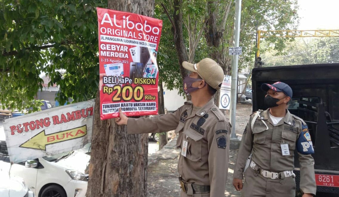 Para petugas Satpol PP sedang menertibkan poster yang di paku di pohon.